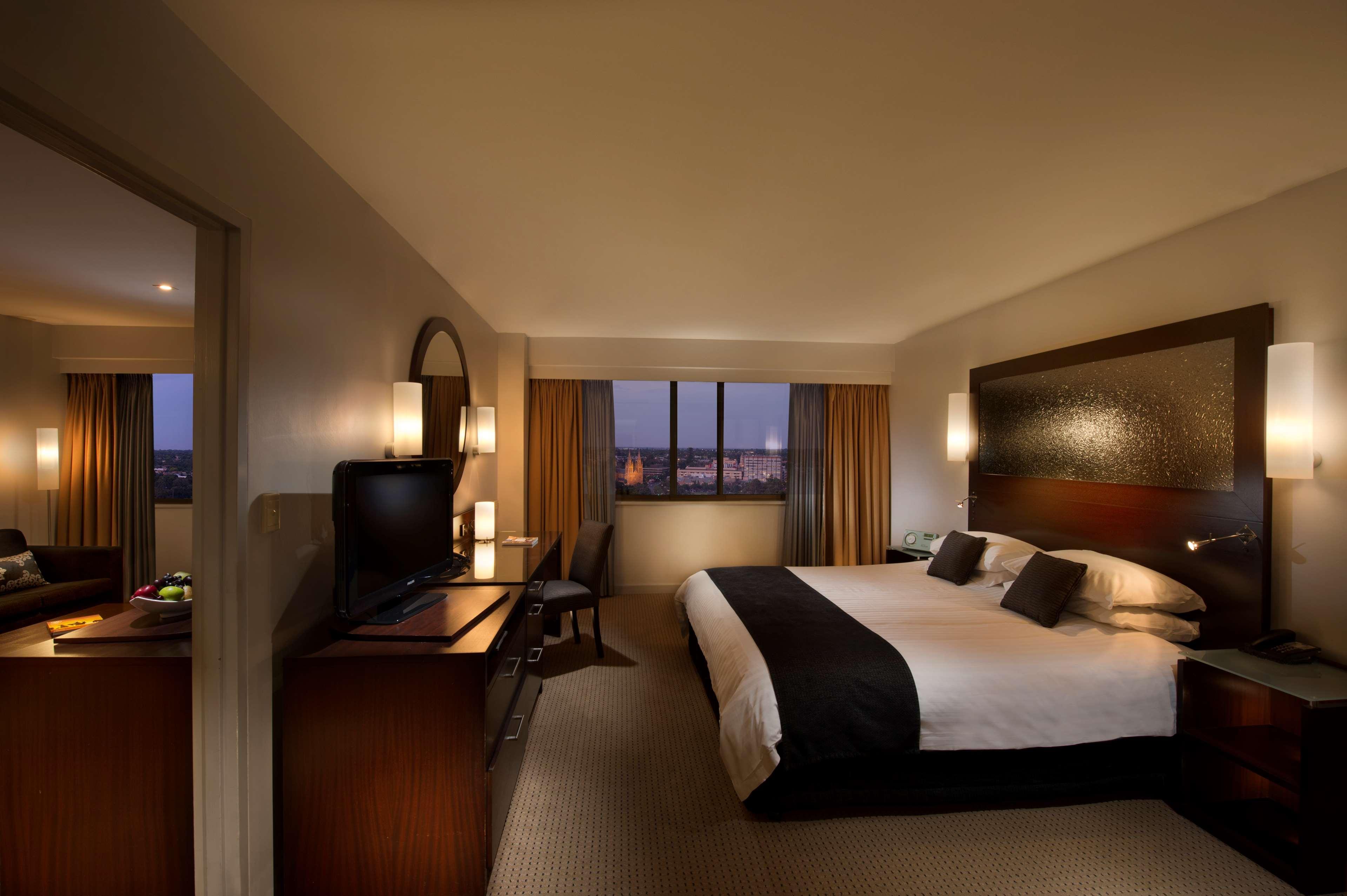 Stamford Plaza Adelaide Hotell Exteriör bild The photo features a modern hotel room that includes a large bed with dark and light bedding, complemented by two pillows. The room is well-lit with warm lighting and has a contemporary aesthetic. To one side, there is a wooden dresser with a flat-sc