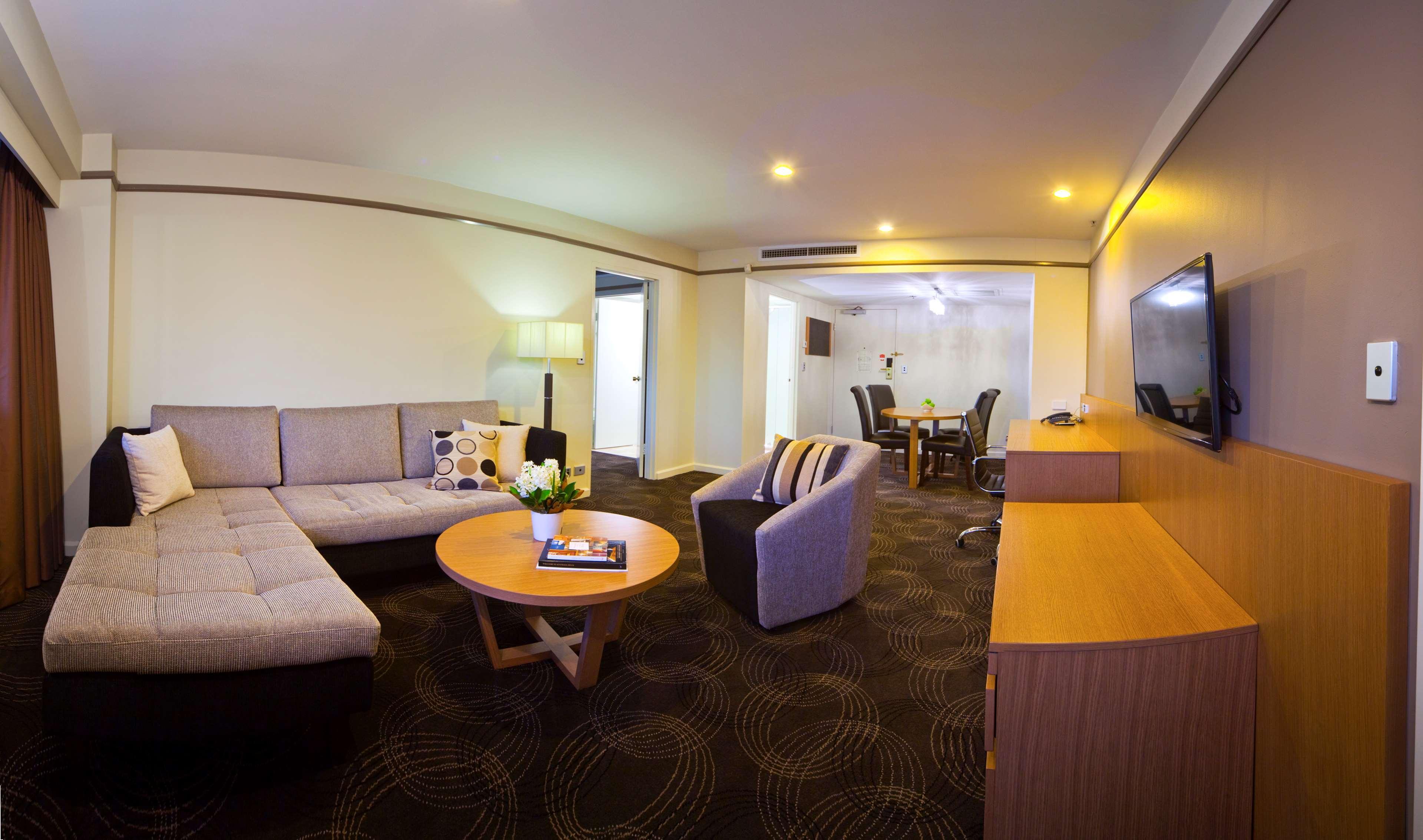 Stamford Plaza Adelaide Hotell Exteriör bild The photo shows a spacious living area with modern decor. On the left, there is a light gray sectional sofa, accompanied by a round wooden coffee table in front of it. A couple of decorative pillows add a touch of color to the sofa. To the right, the