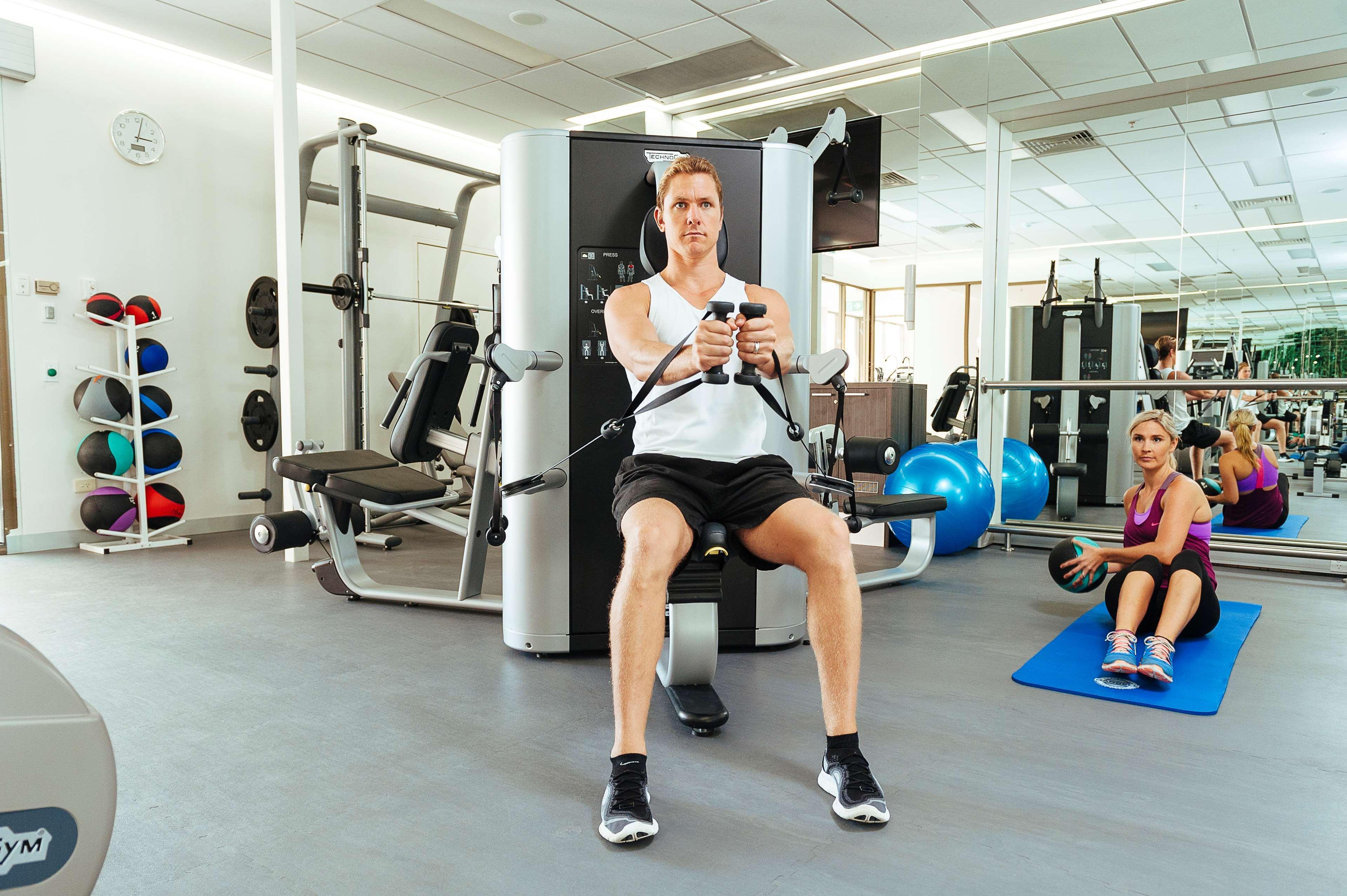 Stamford Plaza Adelaide Hotell Exteriör bild The photo shows a gym setting with two individuals engaged in workout activities. 

In the foreground, a man is seated on a machine, using the handles to perform a rowing exercise. He is wearing a sleeveless shirt and shorts, indicating an active wor