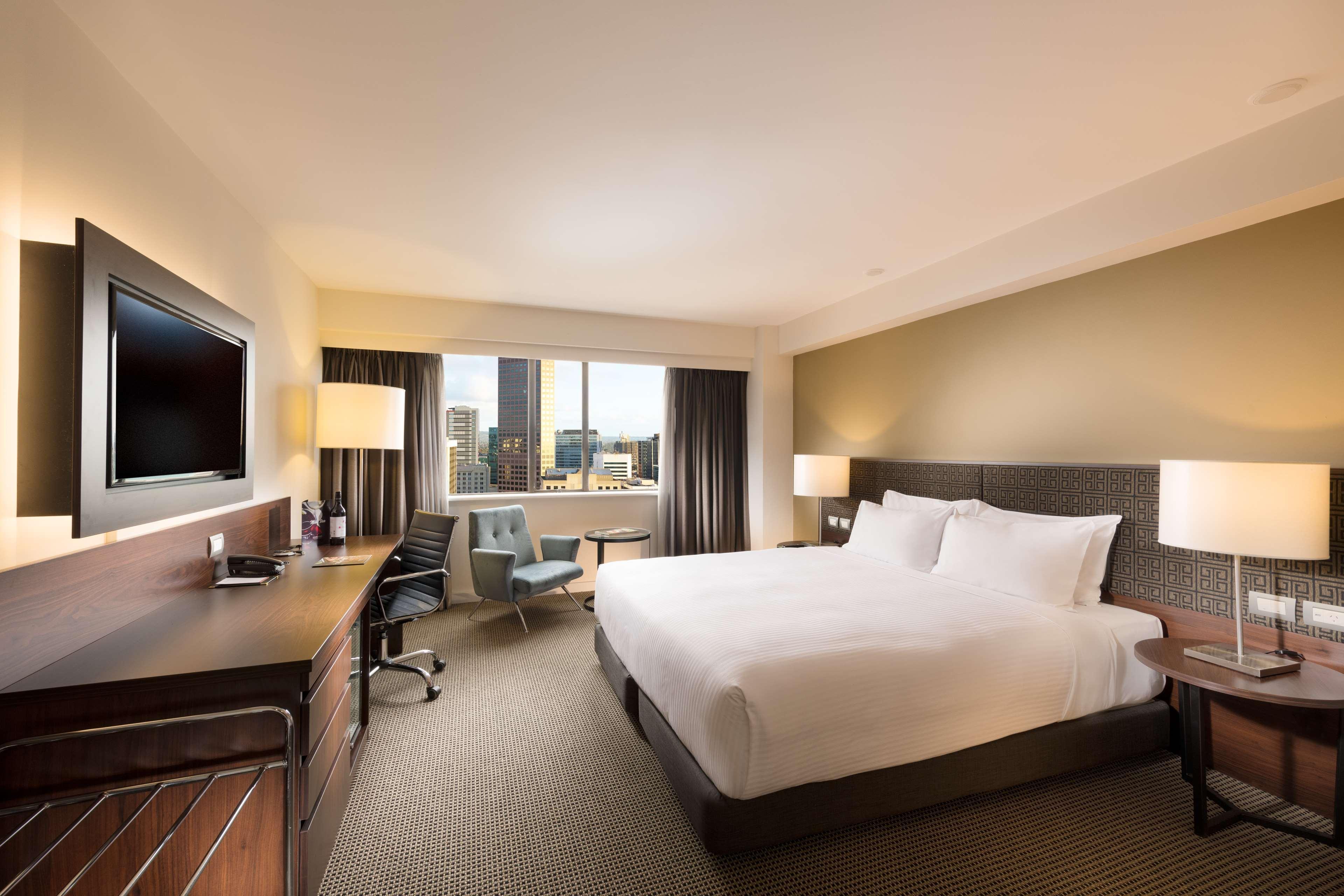 Stamford Plaza Adelaide Hotell Exteriör bild The photo shows a modern hotel room with a contemporary design. It features a large bed with white linens, a bedside table on either side with lamps, and a dark wood accent wall. There's a work desk with an office chair and a flat-screen television m