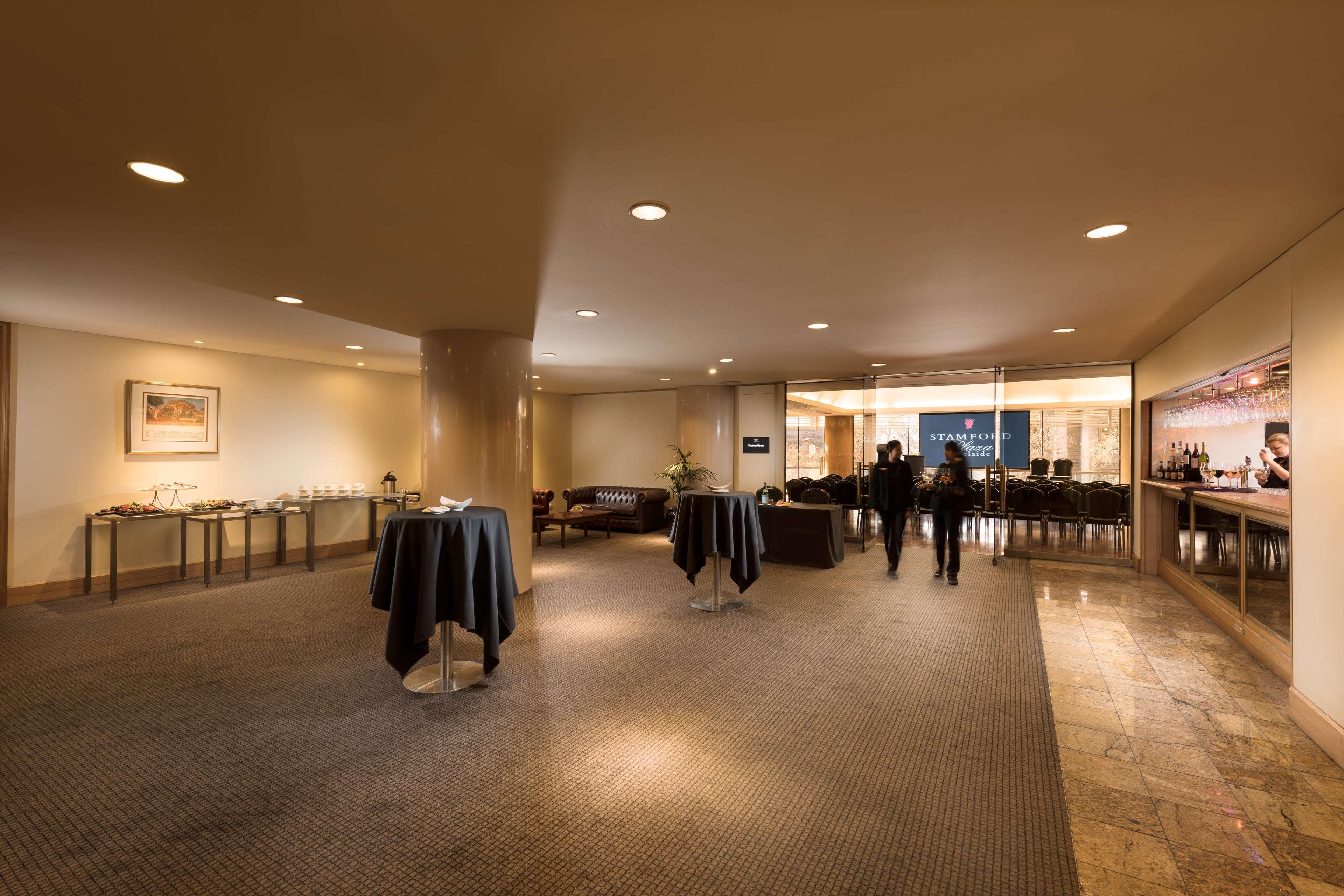 Stamford Plaza Adelaide Hotell Exteriör bild The image shows an indoor space that appears to be a lounge or reception area. There are several round tables with dark tablecloths positioned throughout the room. The floor is carpeted, and the lighting is warm and somewhat dim. In the background, t