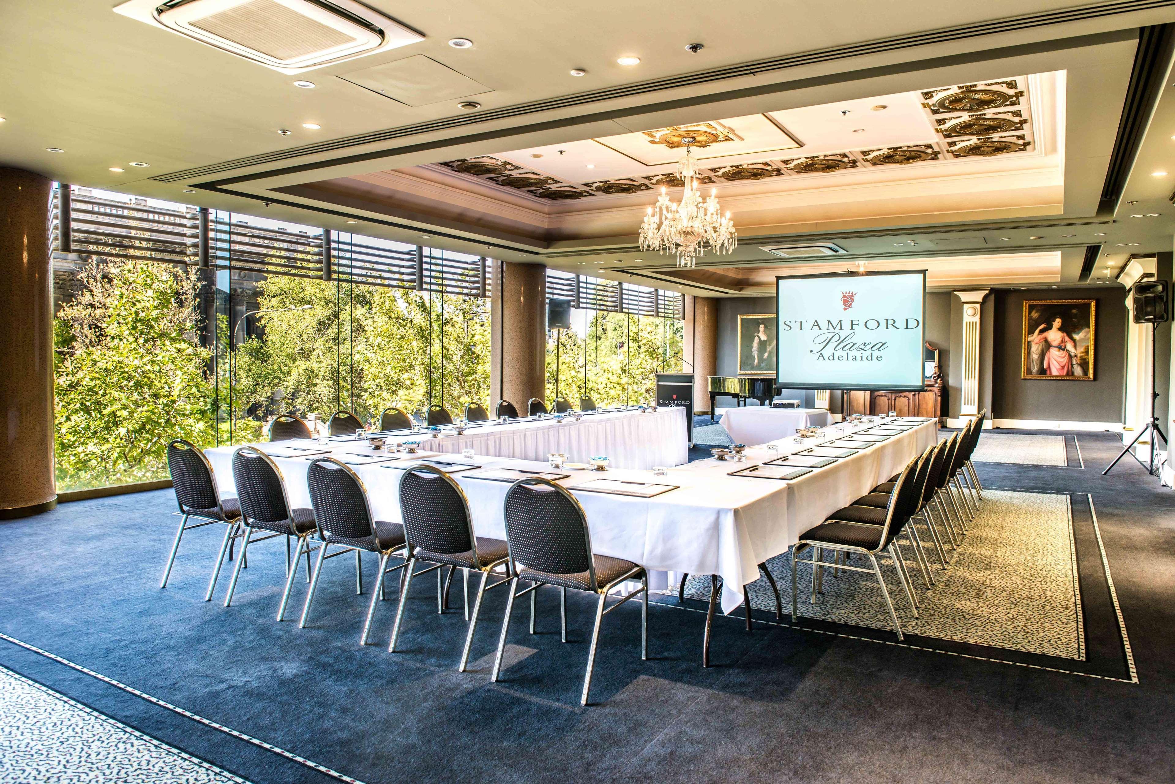 Stamford Plaza Adelaide Hotell Exteriör bild The photo shows a stylish conference room set up for a meeting or event. There is a long rectangular table covered with a white tablecloth, surrounded by black chairs. A large screen displays the name "Stamford" along with a logo. The room features l
